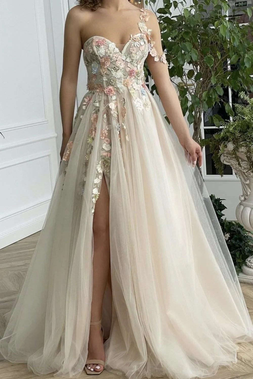 Vestido de fiesta largo color champán con un hombro descubierto y abertura con flores