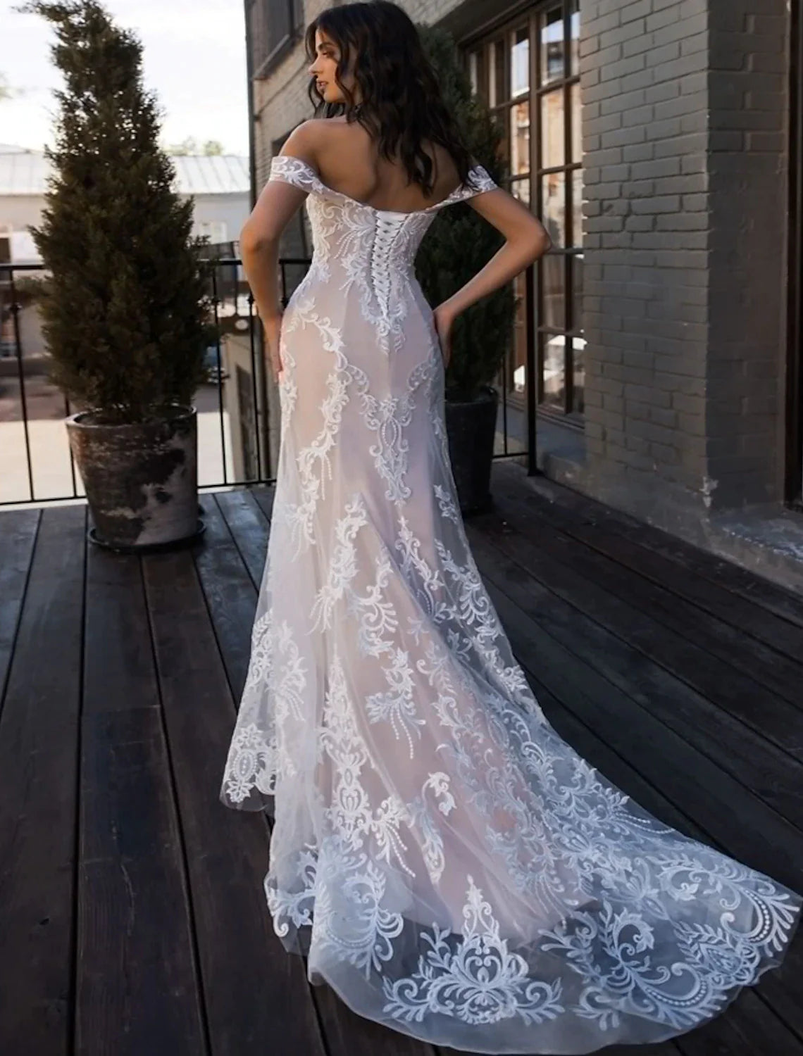 Side view of a bride in a white lace mermaid wedding dress, highlighting the elegant silhouette and flowing train.
