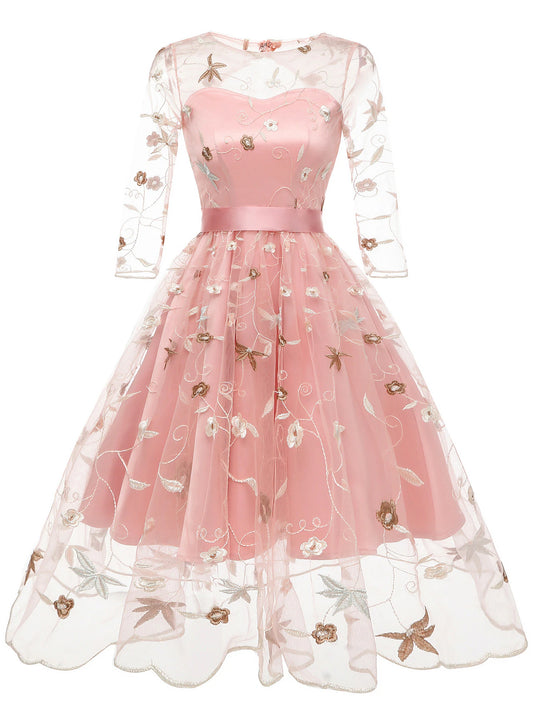 Model wearing an A-line floral tulle cocktail dress with half sleeves and jewel neck.