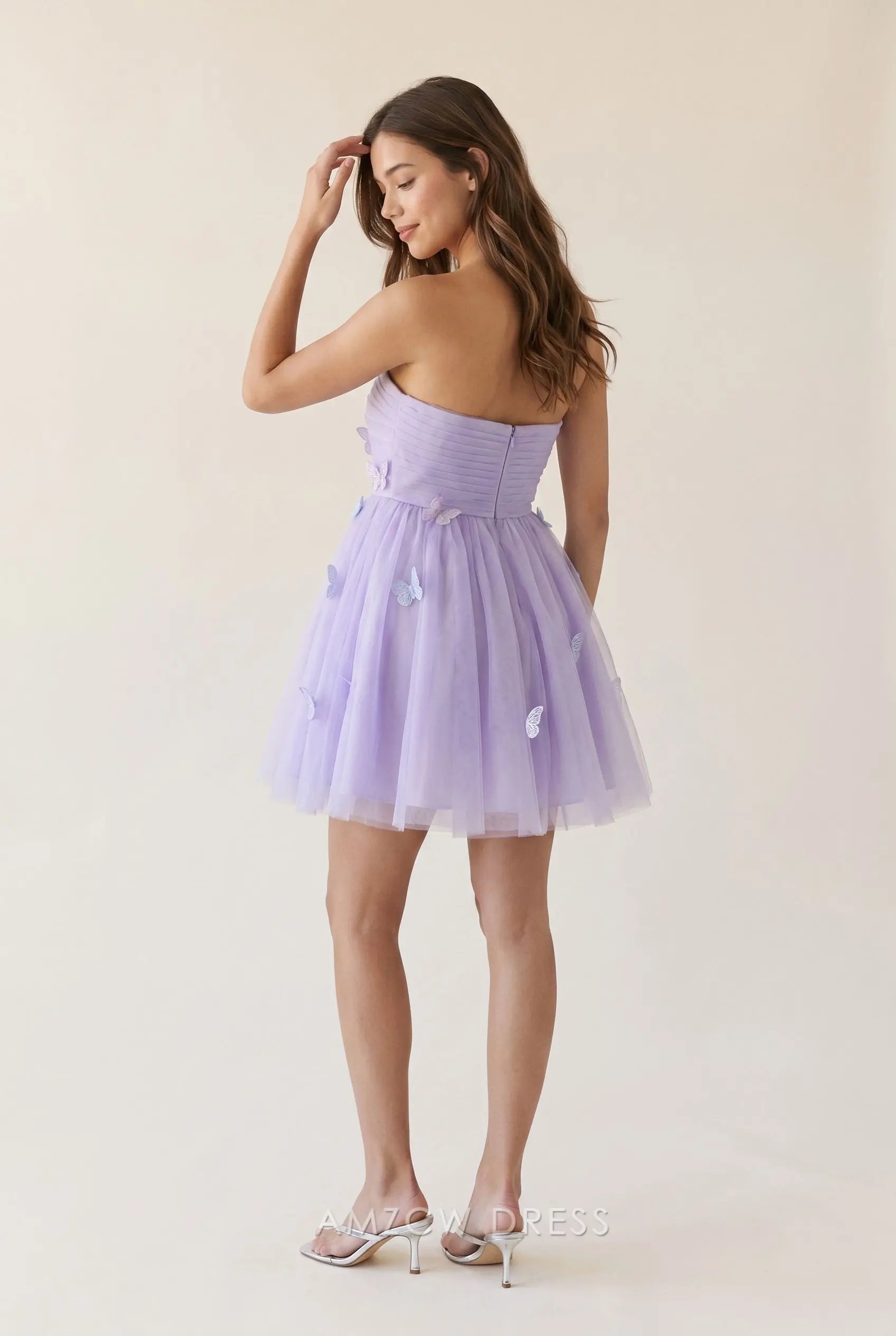 Model showcasing the open back and ruched bustier of a lavender purple strapless mini homecoming dress.