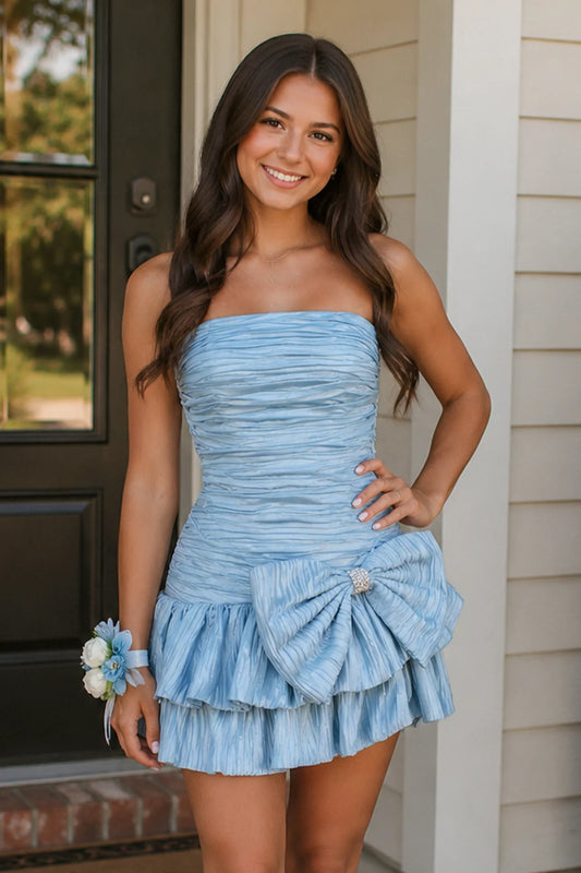 Model wearing a light blue A-line strapless short homecoming dress with a large bow and ruched details.