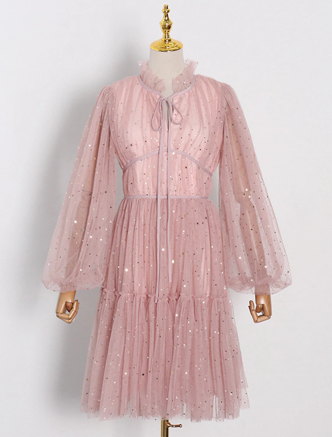 Model wearing a glittering A-line knee-length party dress with long sleeves and a high neck.