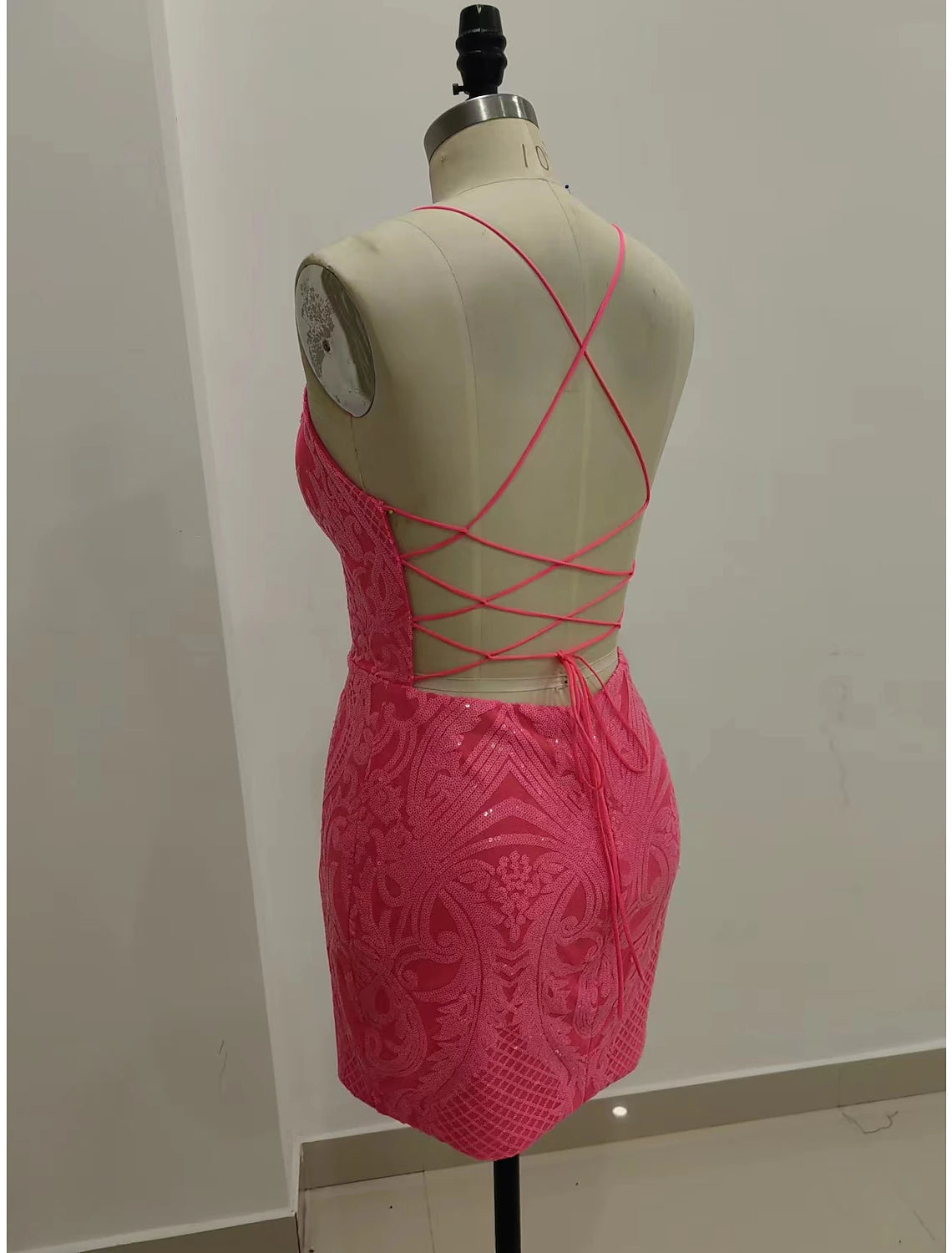 Back view of a model in a sparkling short sequined dress, highlighting the strappy backless design.
