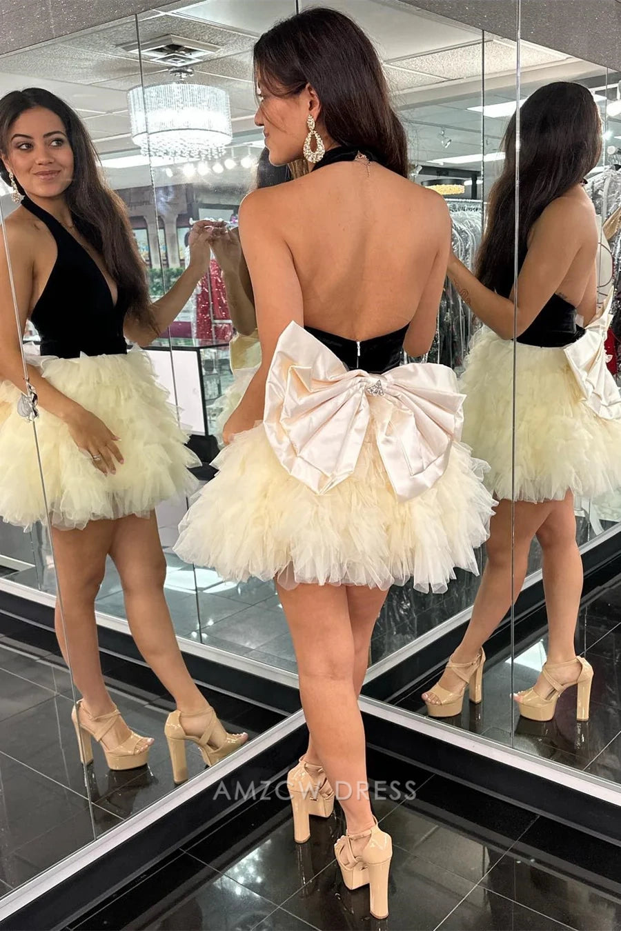 Model posing in the black velvet halter V-neck dress with cream ruffled tulle skirt and back bow.