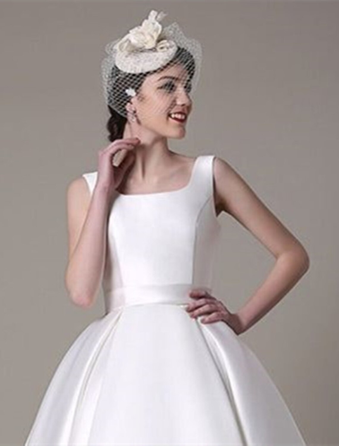 Side view of a model in a sleeveless A-line satin cocktail dress, showing the knee-length and pleats.