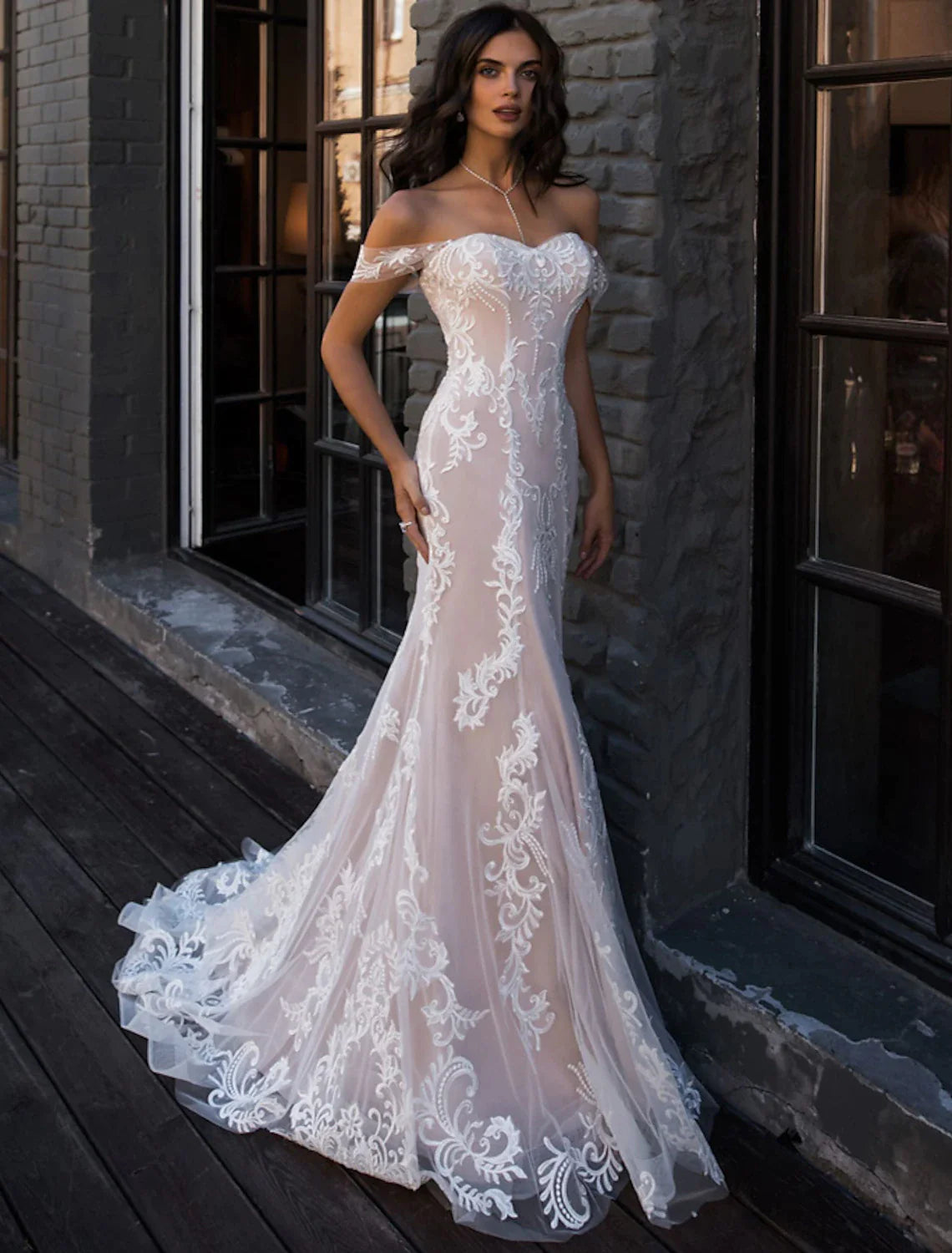 Bride in an elegant white lace mermaid wedding dress with off-shoulder cap sleeves and a court train, posing outdoors.