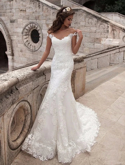 Model wearing an elegant off-shoulder cap sleeve mermaid wedding dress with lace appliques.
