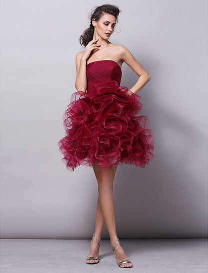 Model wearing a strapless pink tulle ball gown with ruched tiers, posing elegantly.