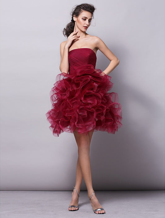 Model wearing a strapless pink tulle ball gown with ruched tiers, posing elegantly.